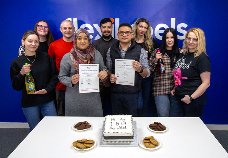 Image shows Flexi Labels Team in front of a cake which reads - we are ISO accredited. The team are holding the certificates for ISO 9001 and ISO 14001.